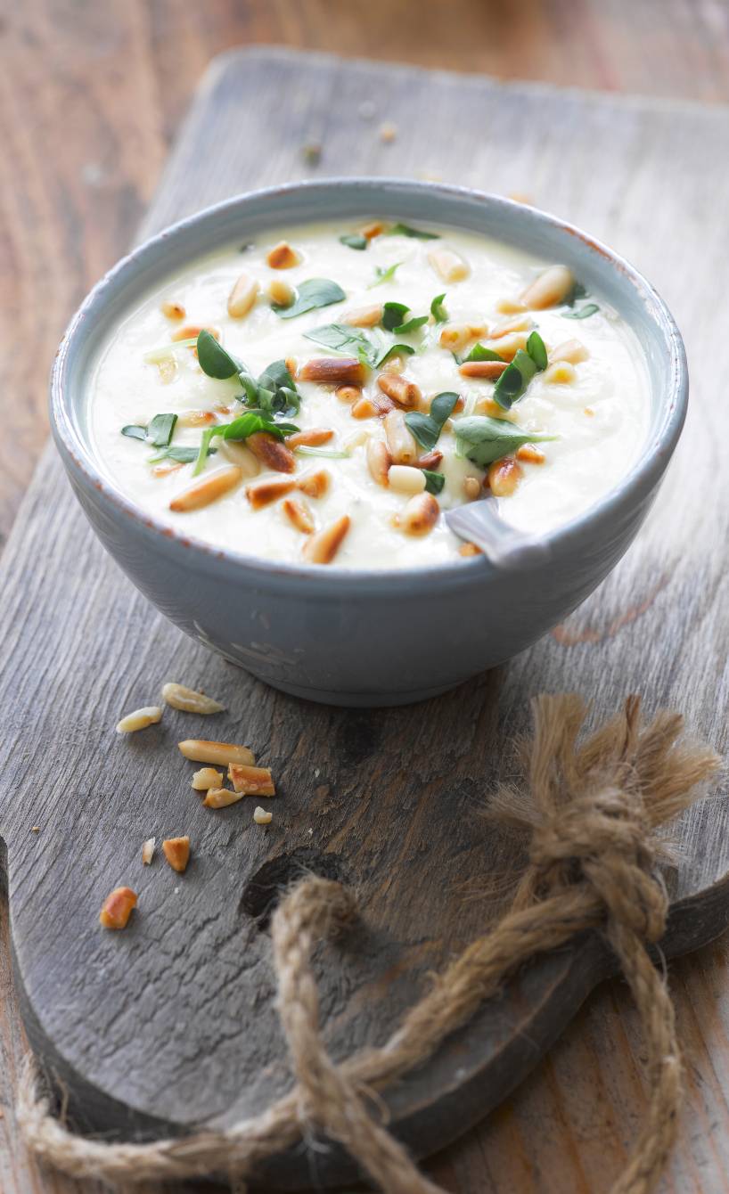 Joghurtdip in einer Schale auf einem Holzbrett getoppt mit Pinienkernen