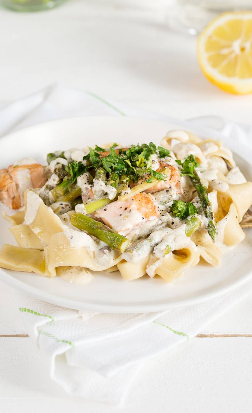 Bandnudeln mit Lachsfilet, grünem Spargel und Sahnesauce auf einem Teller getoppt mit frischer Petersilie