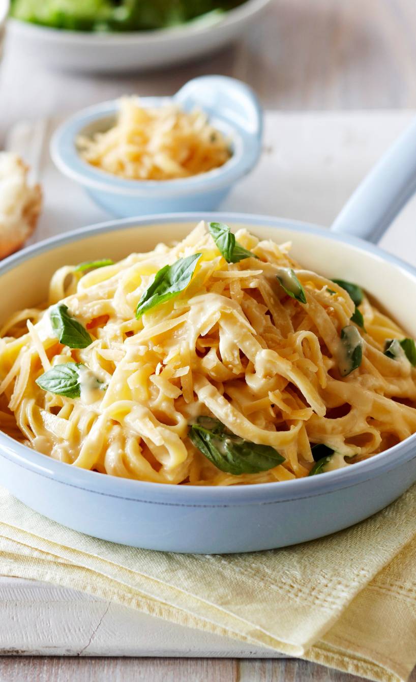 Pasta Alfredo in einer Stielpfanne getoppt mit Käse und frischem Basilikum
