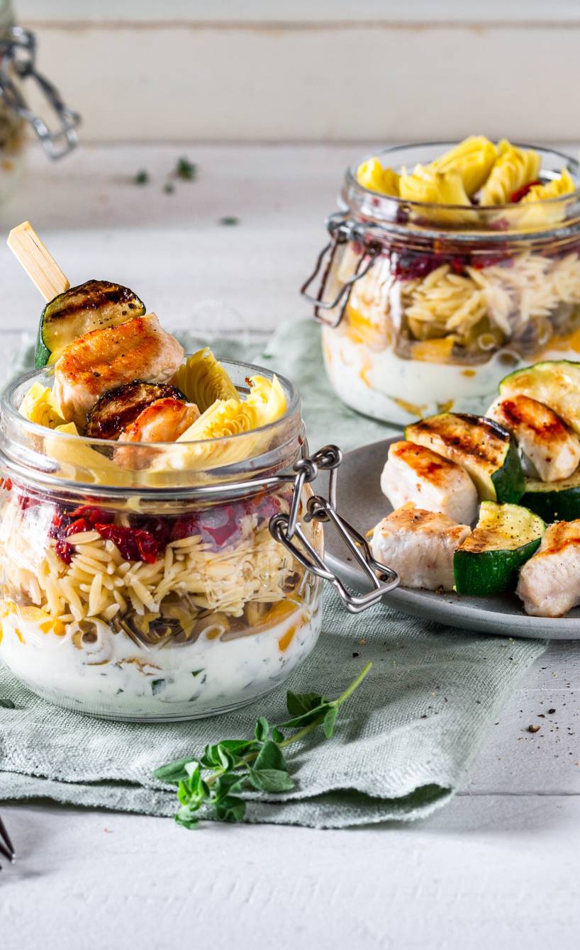 Pastasalat im Glas geschichtet, darauf Spieße mit gegrilltem Hähnchen und Zucchini