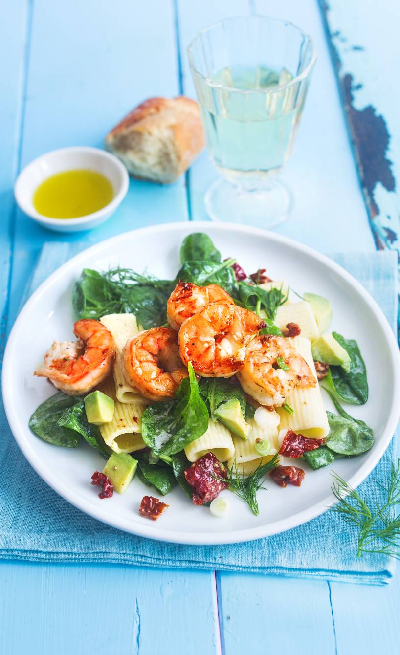 Pastasalat auf einem Teller getoppt mit mit gebratenen Garnelen, Spinat und Avocadostücken, daneben Joghurtdressing in einer Schale