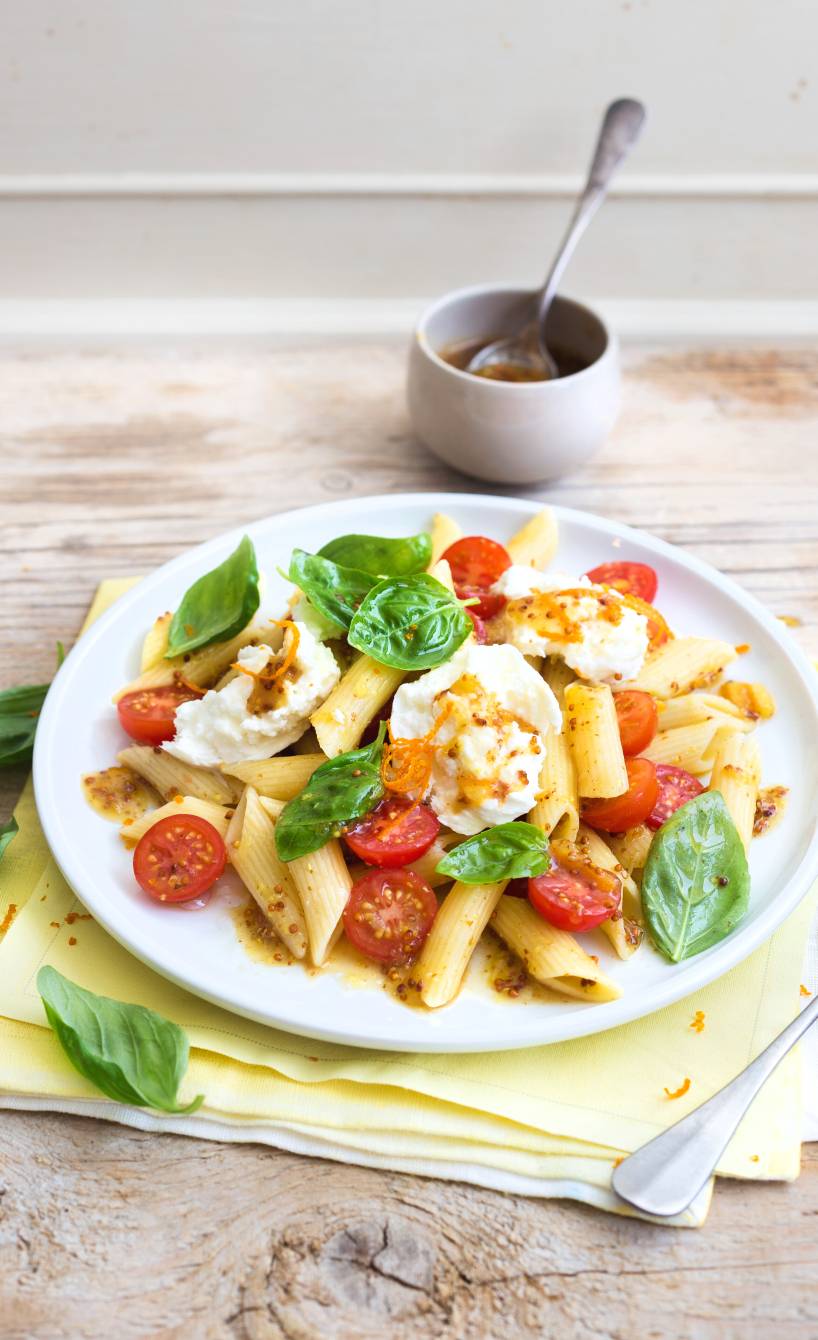 Pastasalat aus Röhrennudeln auf einem Teller, darauf Kirschtomaten, Mozzarella und Orangen-Senf-Dressing in einer Schüssel daneben