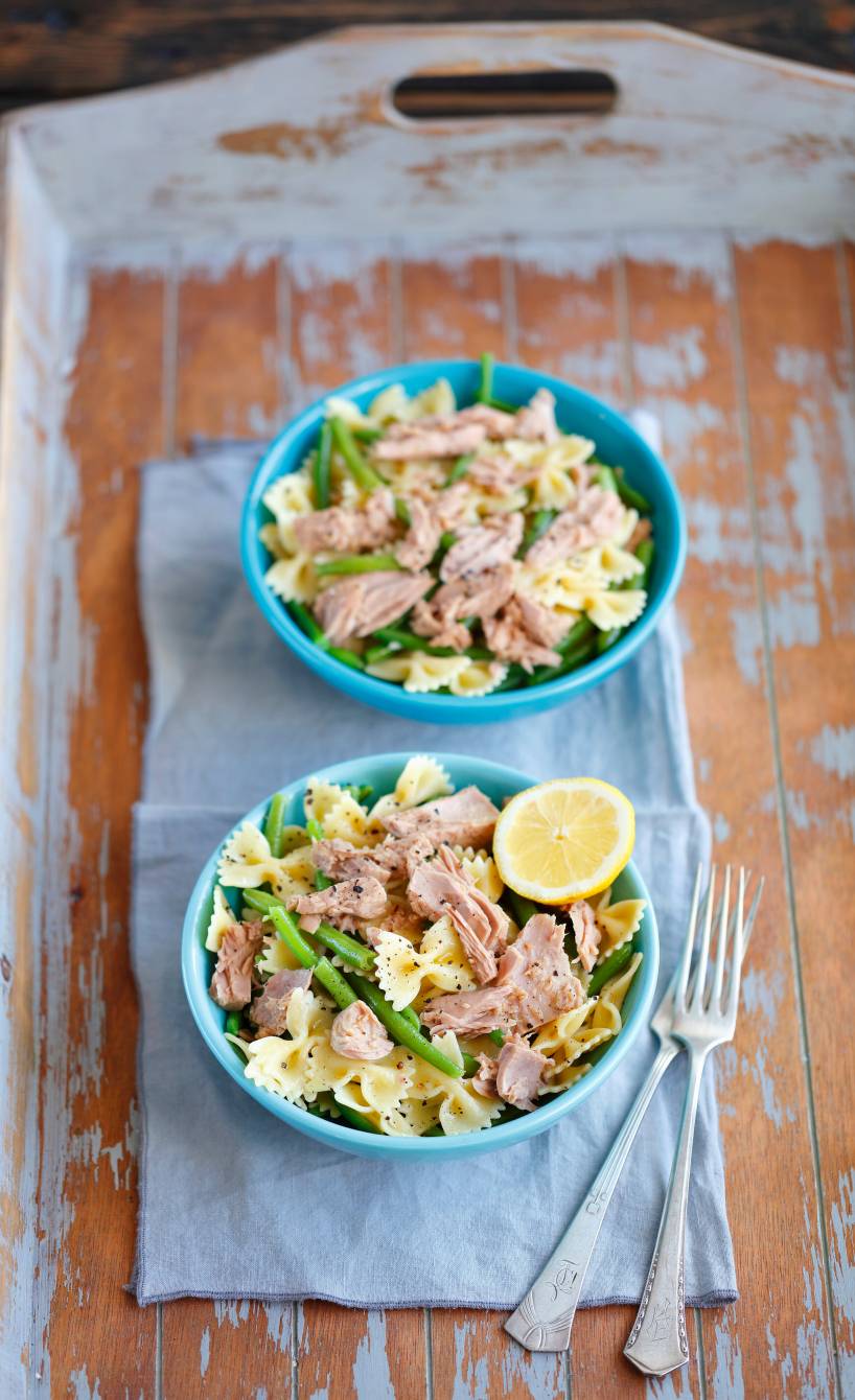 Pastasalat in einer Schüssel auf einem Tisch mit Thunfisch, grünen Bohnen und garniert mit einer halbe Zitrone