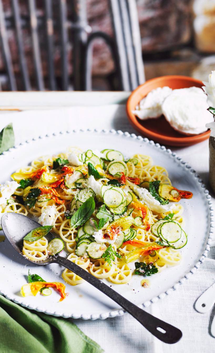 Pastasalat mit Zucchini und Zucchiniblüten auf einem Teller, getoppt mit Mozzarella, Basilikum und Minze