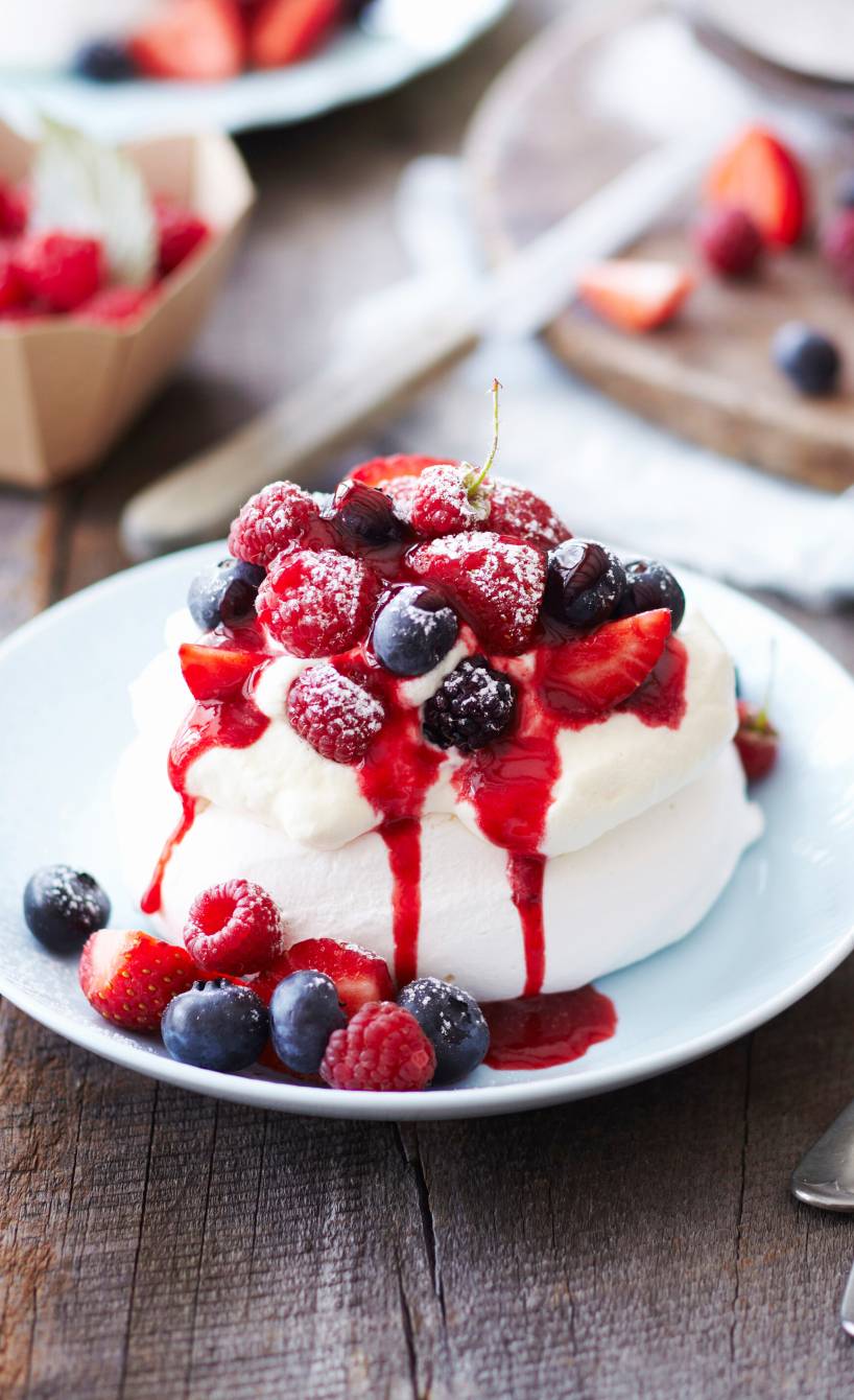 Mini-Pavlova mit frischen Beeren und Himbeeressigsauce auf einem Dessertteller