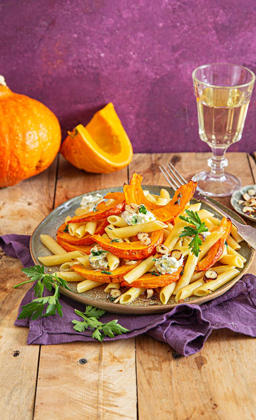 Penne auf einem Teller mit Ofenkürbis-Spalten und Ziegenkäsecreme getoppt