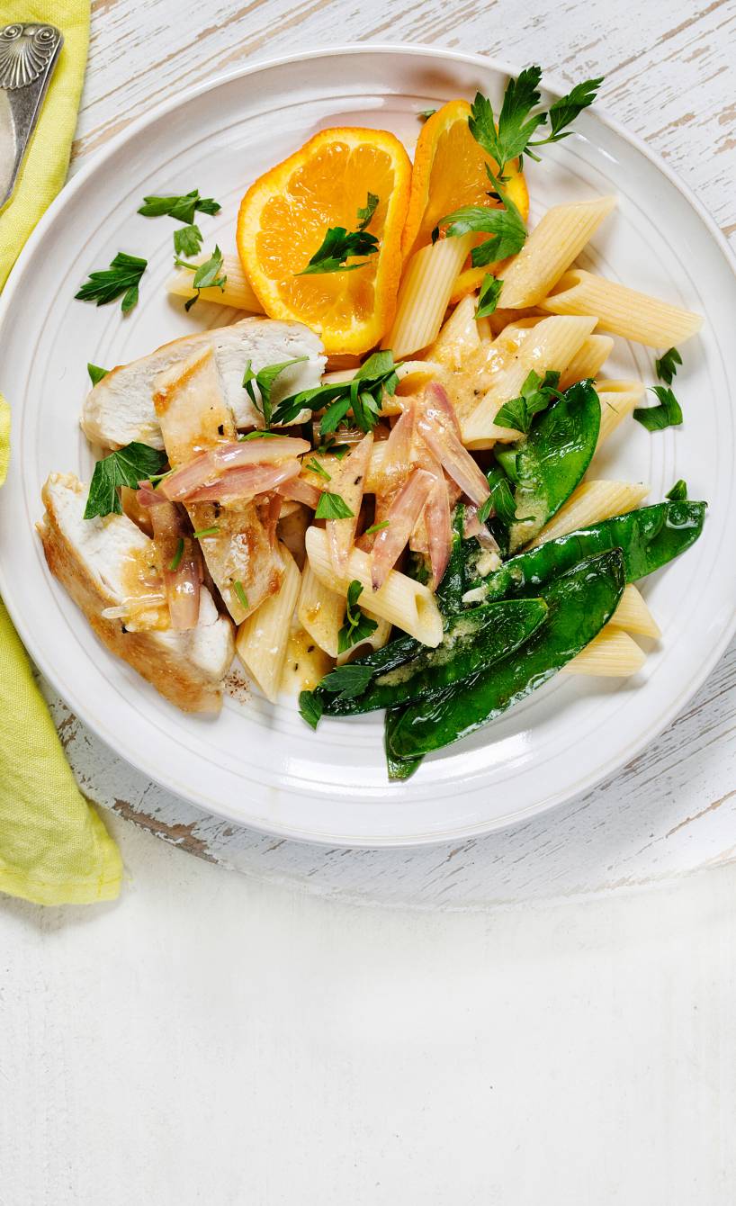 Hähnchenbrustfiletstreifen angerichtet mit  Ricotta-Orangensauce, Penne, Zuckerschoten und Orangenscheiben auf einem Teller