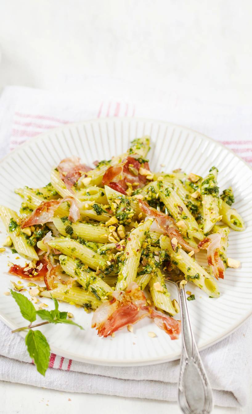Penne mit Pistazienpesto und gebratenem Pancetta auf einem Teller angerichtet