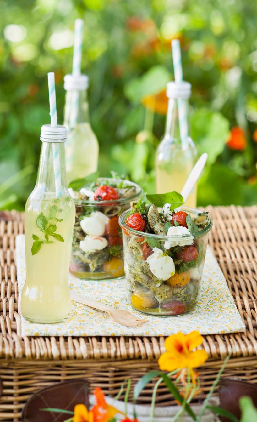 Nudelsalat in zwei Gläsern auf einem Gartentisch, daneben zwei Flaschen Limonade