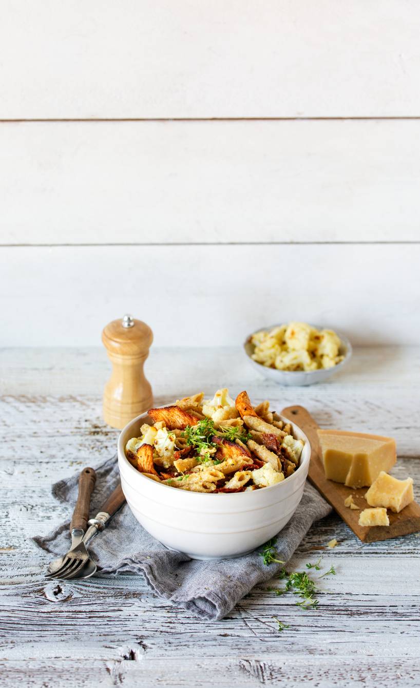Salat mit Vollkornpenne in einer Schüssel getoppt von Hähnchenstreifen, daneben ein Stück Parmesan