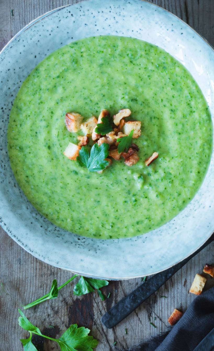 Wirsingcremesuppe in einem Teller getoppt von Croûtons, Nüssen und frischer Petersilie auf einem Tisch von oben