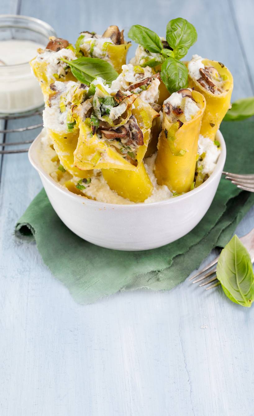 Cannelloni mit Champignon-Lauch-Ricotta-Füllung aufrecht angerichtet in einer Schale garniert mit frischem Basilikum