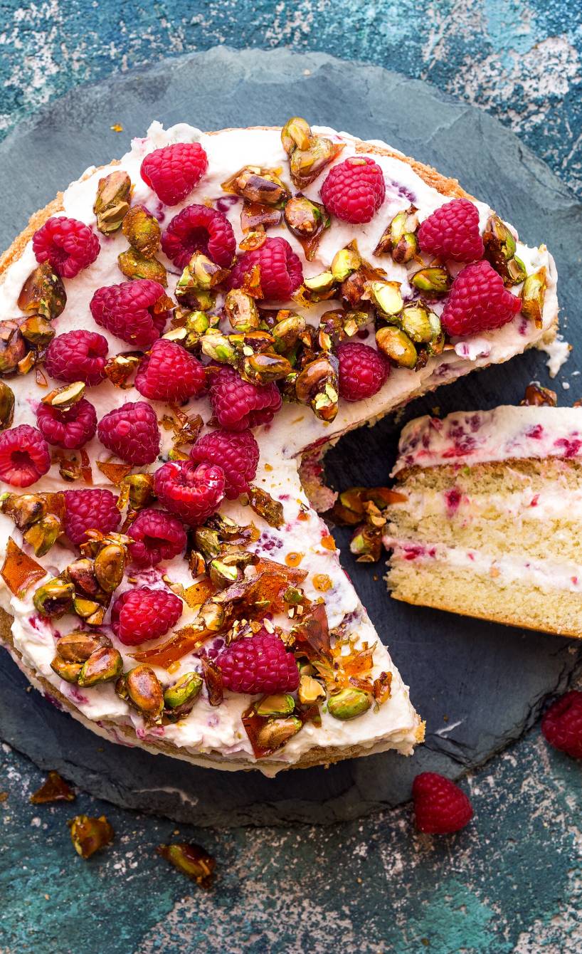 Pistazien-Himbeer-Torte angeschnitten auf einer Tortenplatte garniert mit frischen Himbeeren und Pistazienkernen