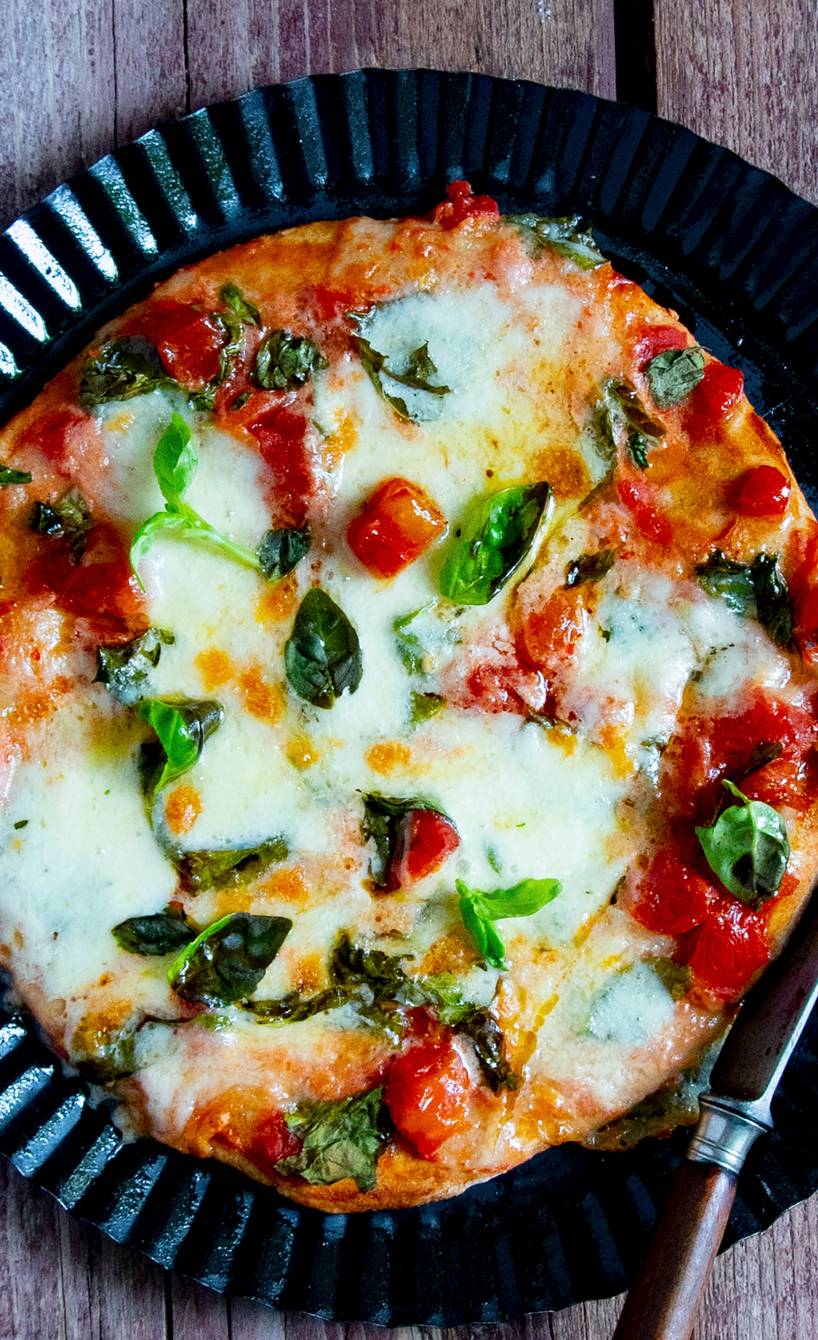 Pizza Margherita aus der Pfanne auf einem schwarzen Pizzateller auf einem Holztisch