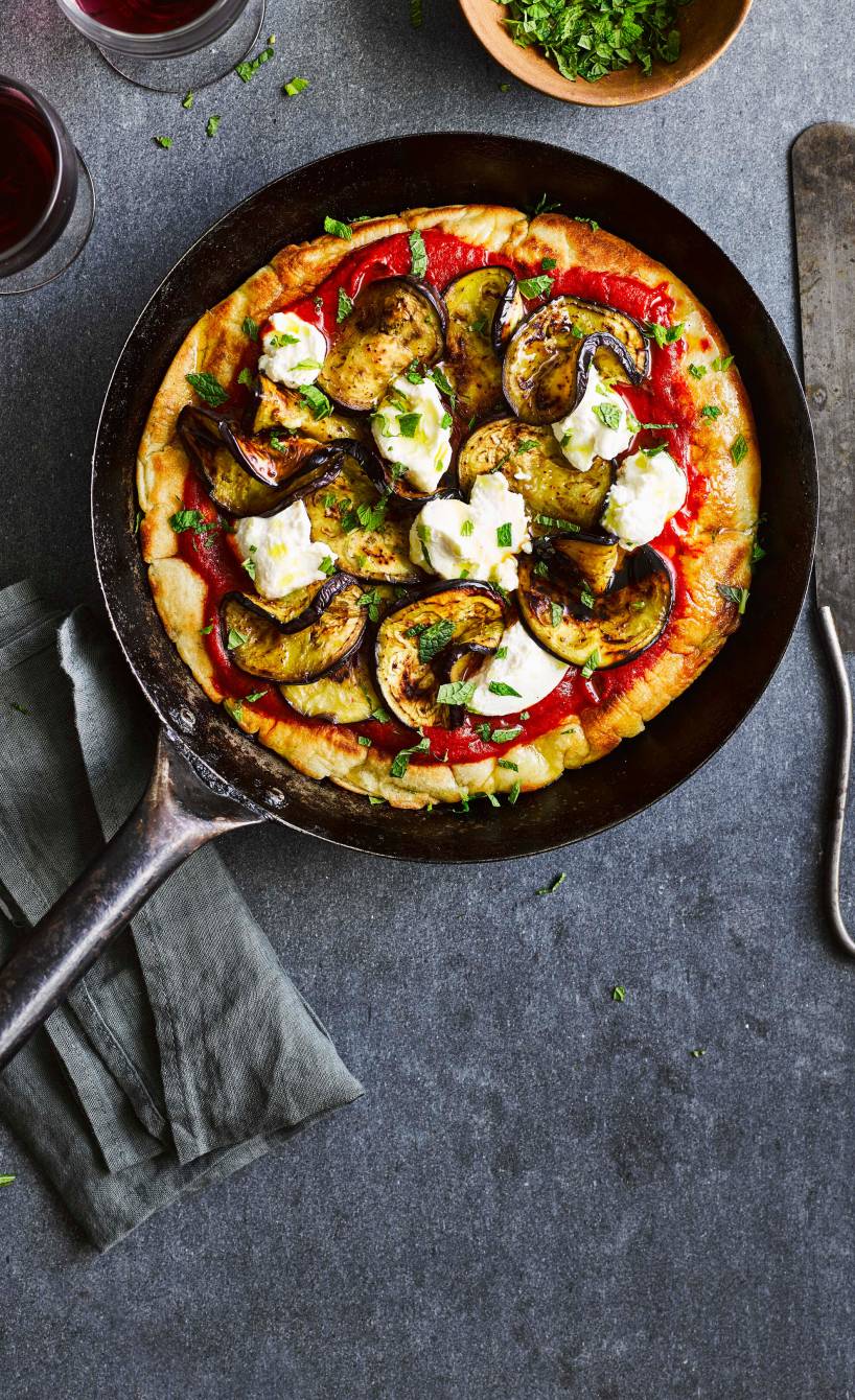 Pizza in einer Pfanne belegt mit Aubergine, Ricotta und Minze