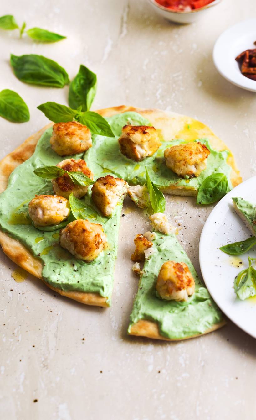 Runde Pizza mit Basilikumcreme und Fischbällchen angeschnitten auf einem Tisch