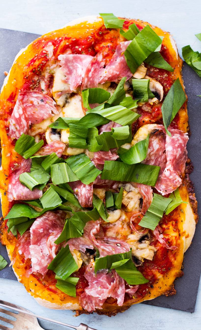 Pizza belegt mit Champignons, Salami und frischem Bärlauch auf einem Schieferbrett
