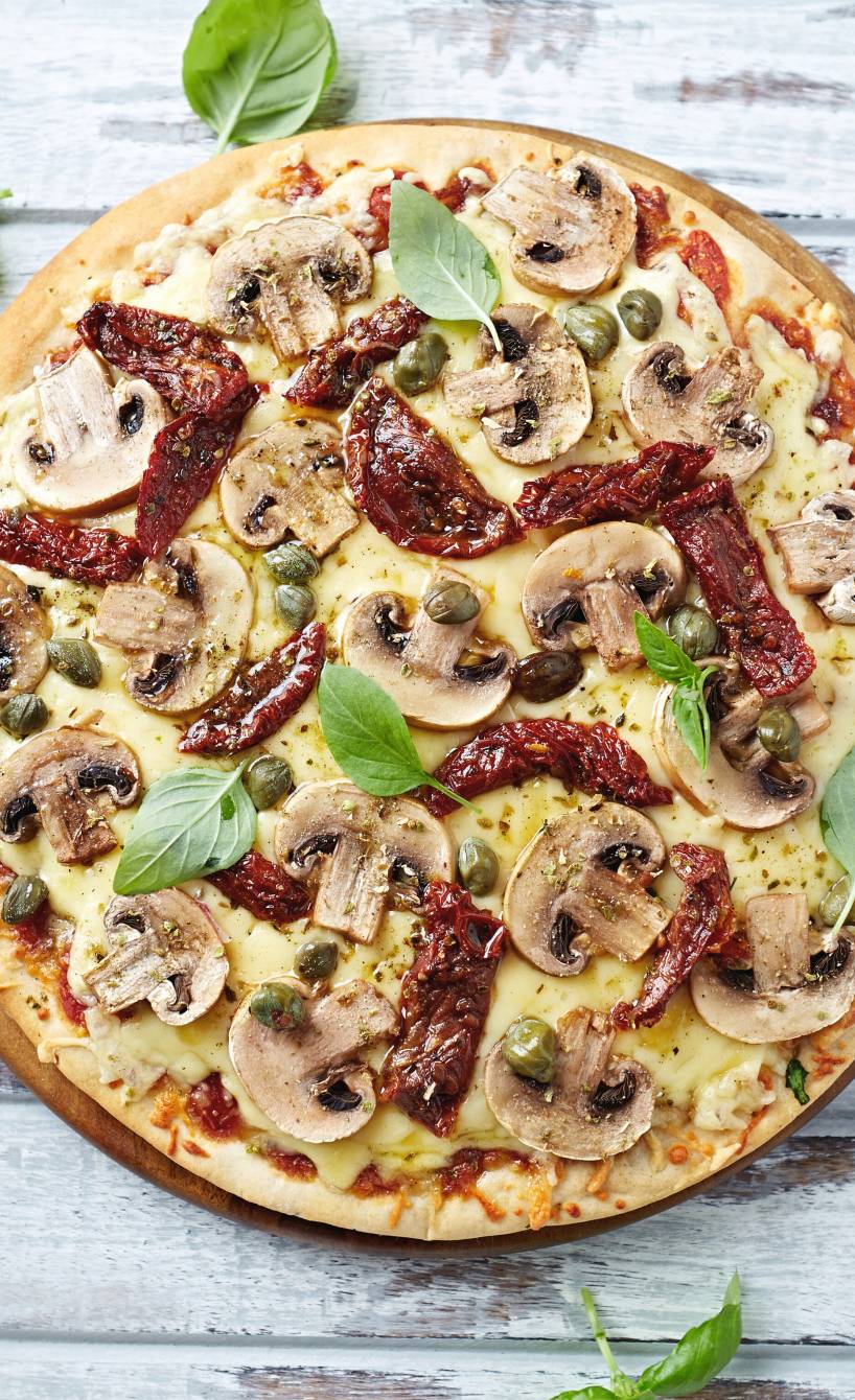 Runde Pizza Funghi auf einem Pizzabrett garniert mit frischem Basilikum