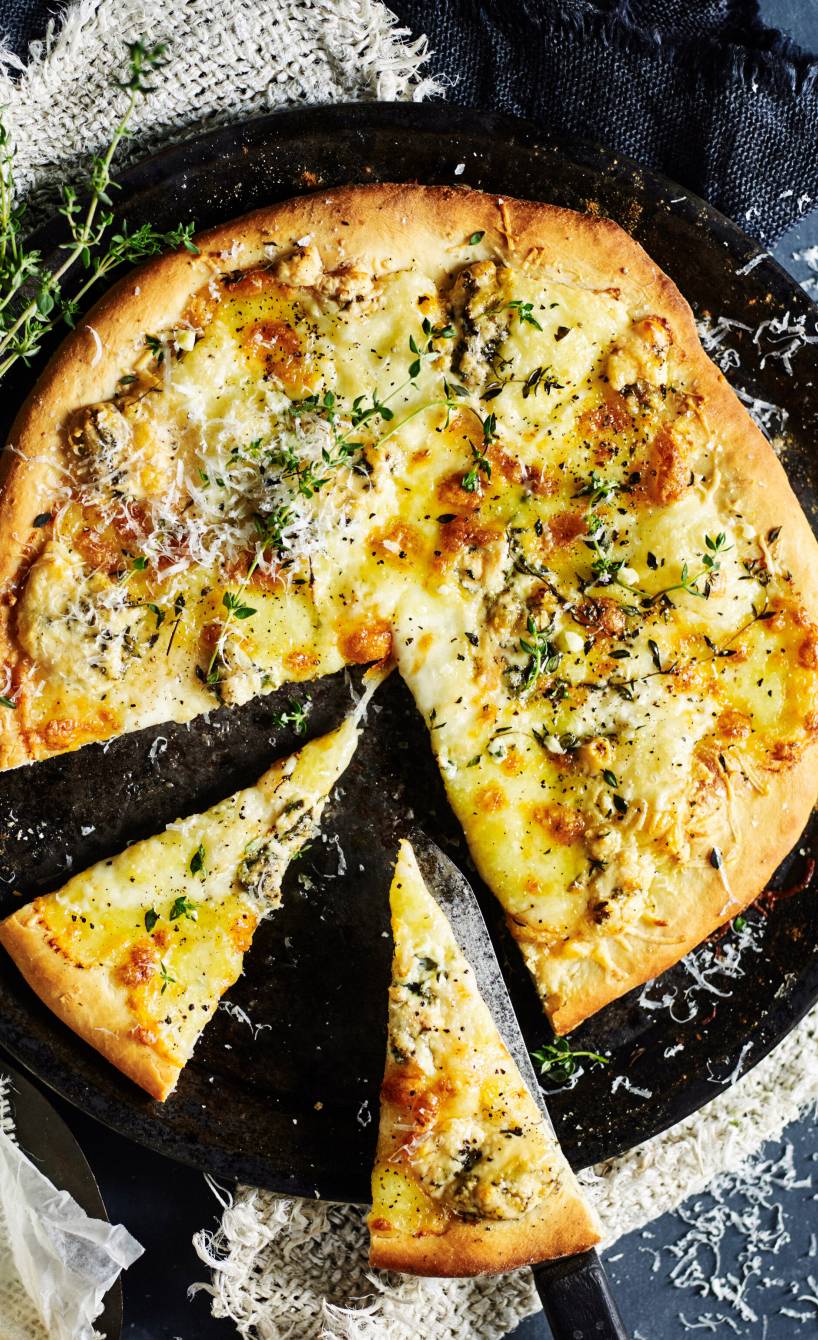 Runde Pizza quattro formaggi angeschnitten auf einem Teller, daneben mehrere Käsesorten
