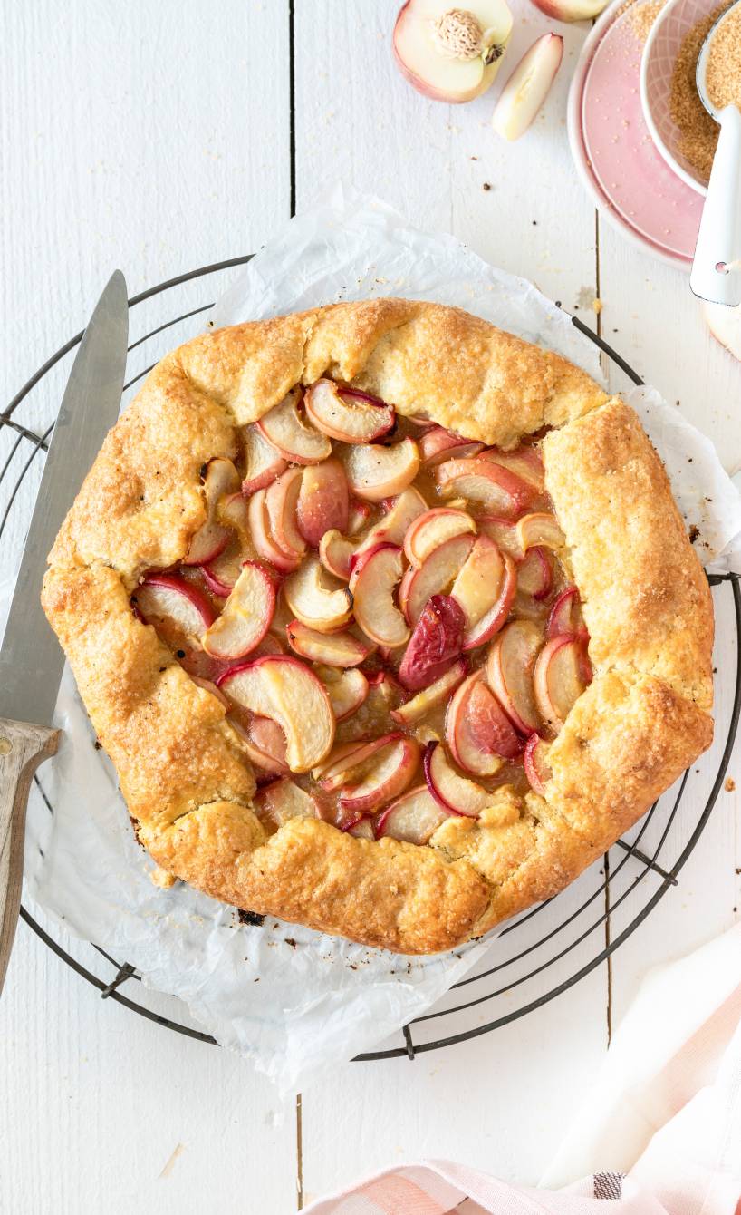 Eine gebackene Pfirsich-Crostata mit Polenta-Teig auf einem Kuchengitter auf einem Holztisch