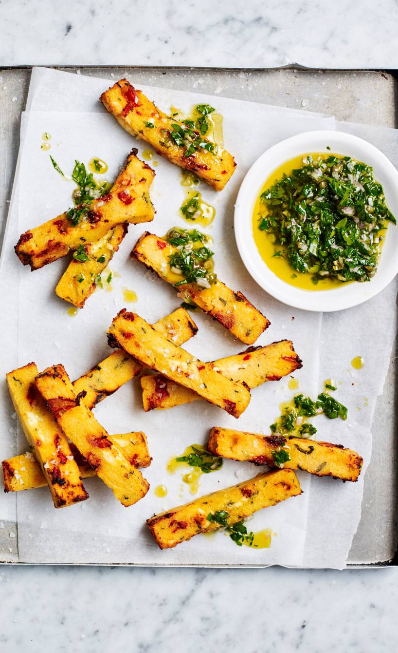 Goldbrauen gebackene Polenta-Pommes mit Feta auf einem Backblech getoppt von grüner Kräuter-Salsa