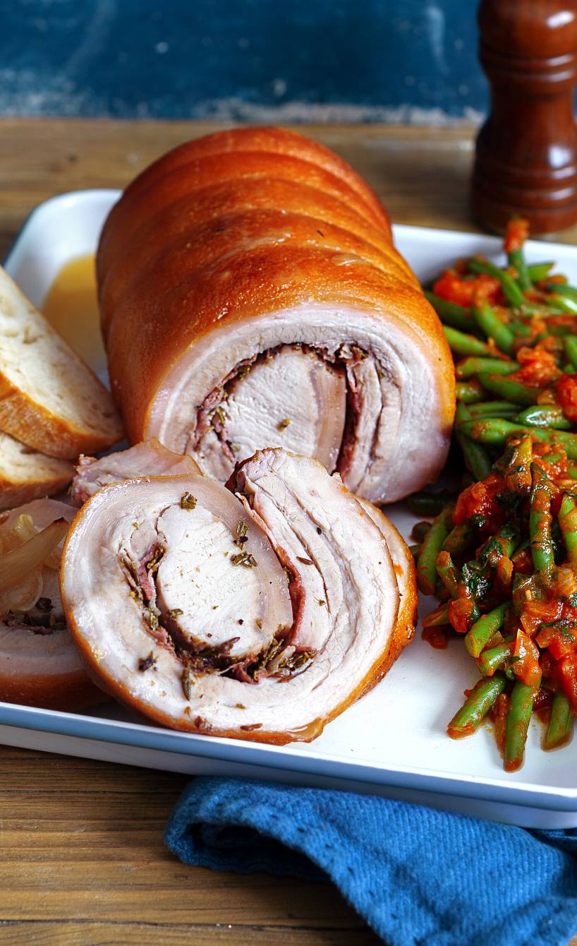 Porchetta, gefüllter Schweinerollbraten auf einem rechteckigen Teller, daneben Bohnengemüse