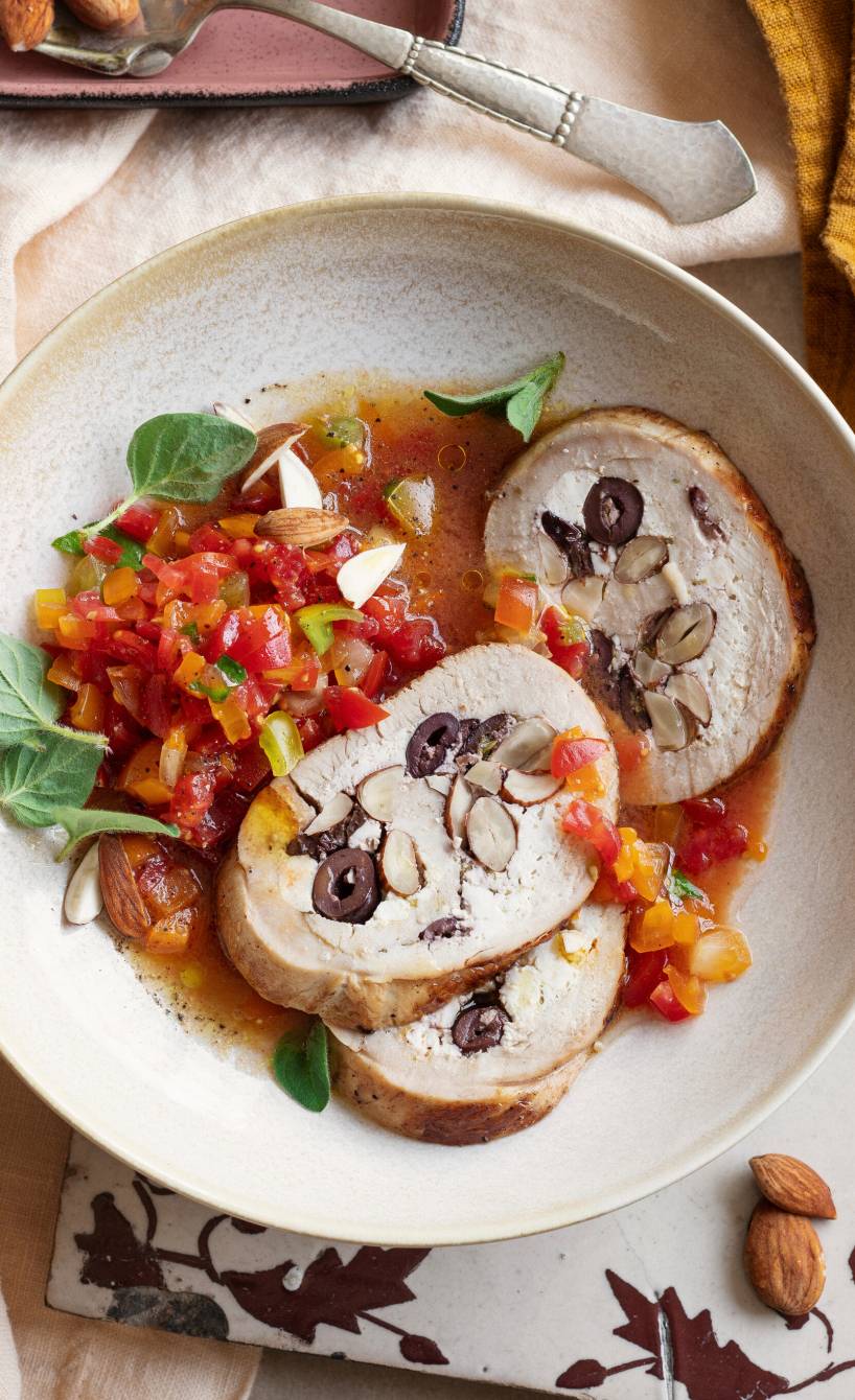 Putenrollbraten mit Ricottafüllung in Scheiben geschnitten auf einem Teller, daneben buntes Gemüse aus dem Bräter