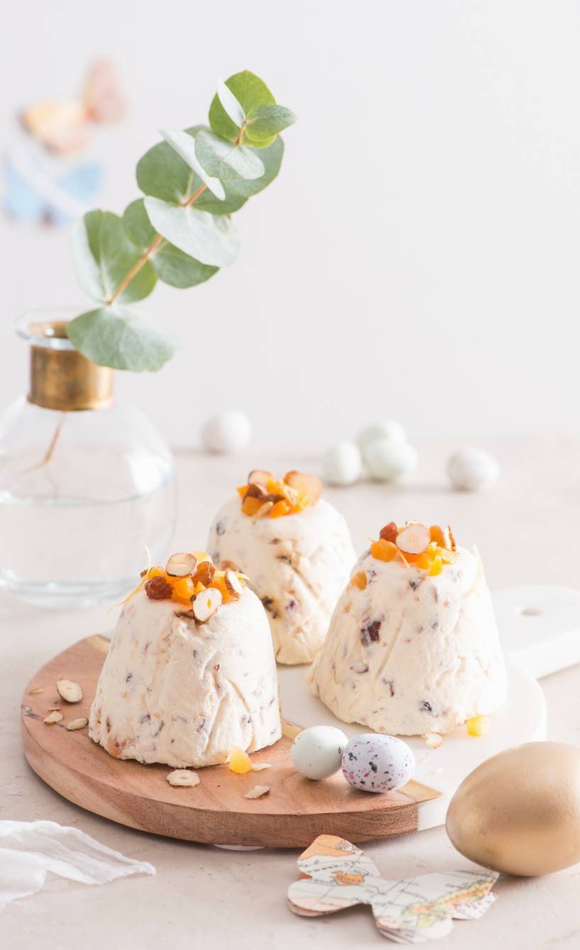 Drei Quark-Desserts in Törtchenform mit Trockenfrüchten und Nüssen auf einem runden Holzbrett mit Osterdeko