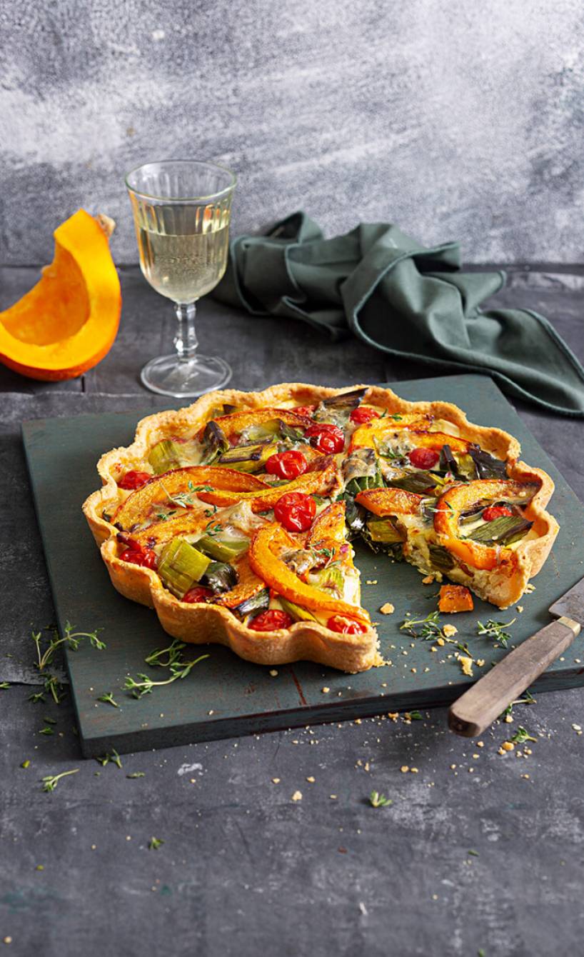 Kürbisquiche angeschnitten auf einer Schieferplatte, dahinter ein Stück Hokkaido