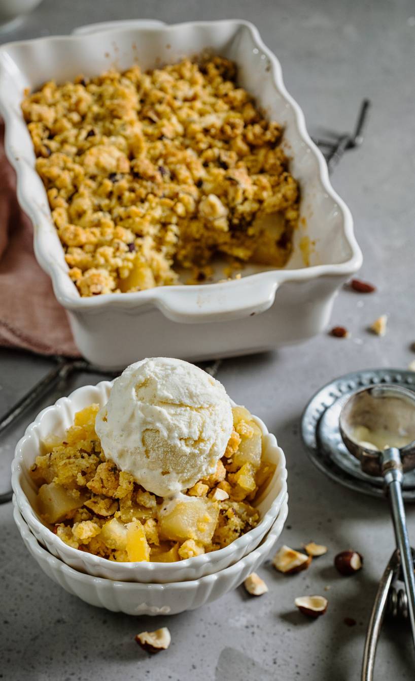 Quitten-Apfel-Crumble mit Haselnüssen und Vanilleeis auf einem Tisch
