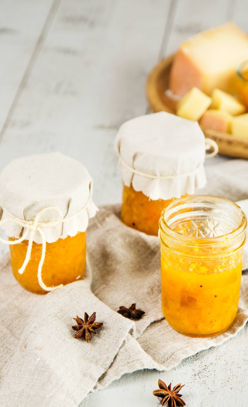 Quittenmarmelade in Einmachgläsern auf einem Tisch, daneben Kürbis und Käse