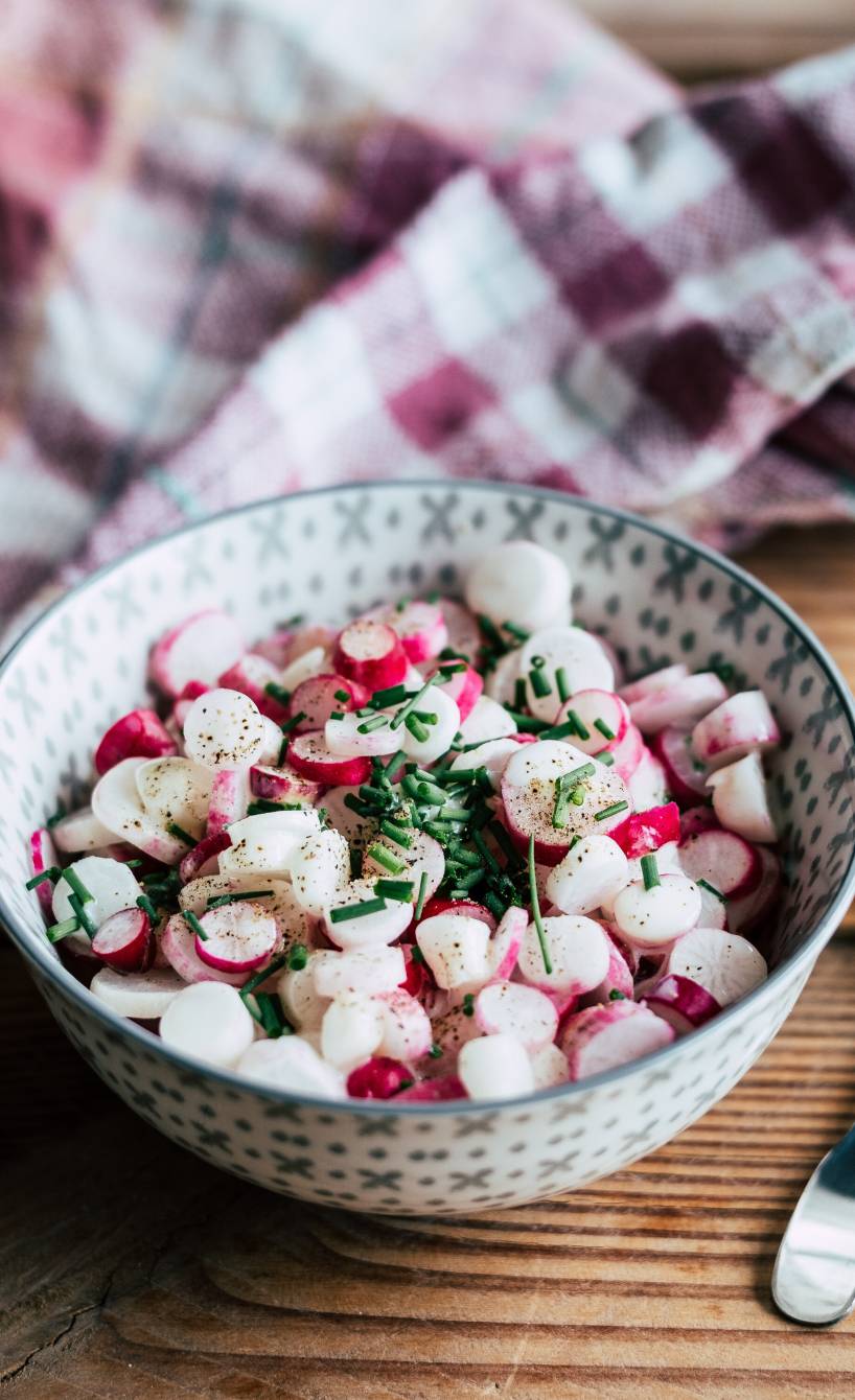 Radieschensalat in einer Salatschüssel getoppt mit Joghurt-Dressing auf einem Tisch