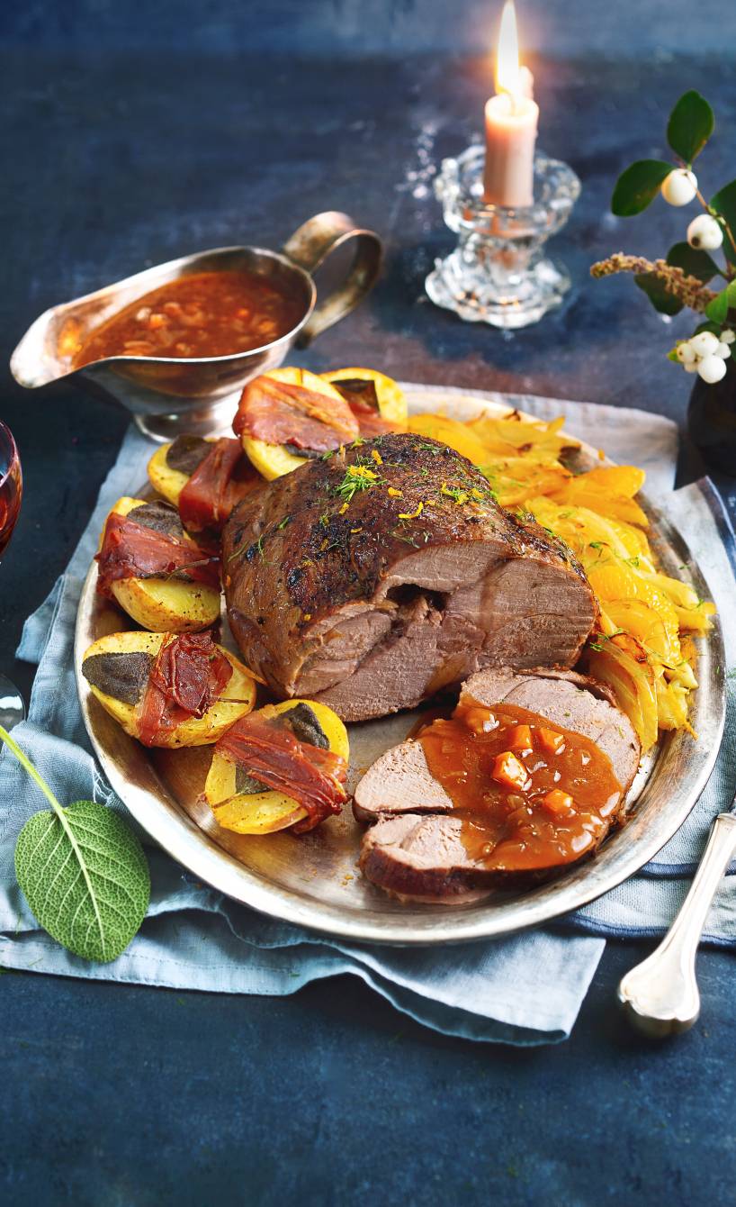 Geschmorter Rehbraten angerichtet auf einer Servierplatte umgeben von Saltimbocca-Kartoffeln, Fenchelgemüse und Rotweinsoße