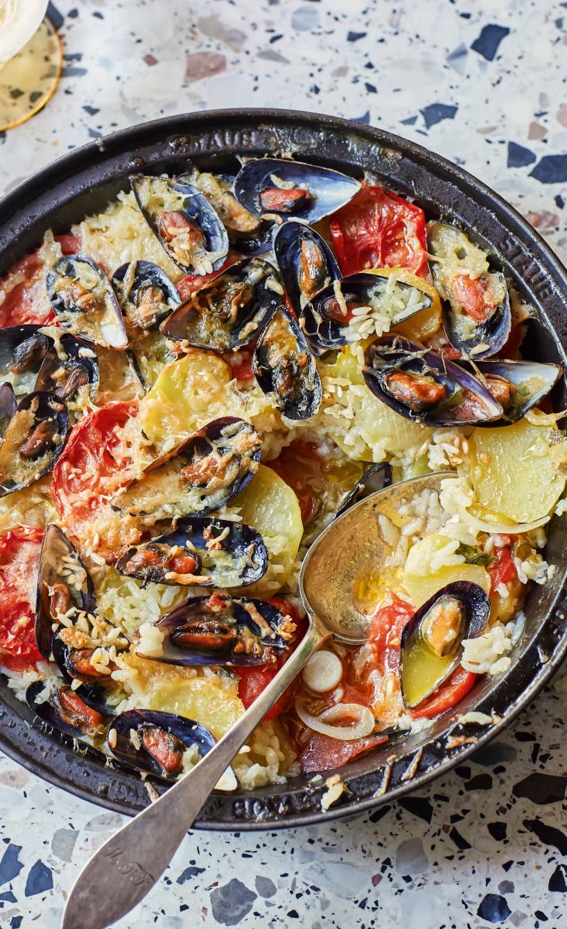 Reis-Kartoffel-Auflauf nach apulischer Art mit Muscheln in einer runden Auflaufform auf einem Tisch