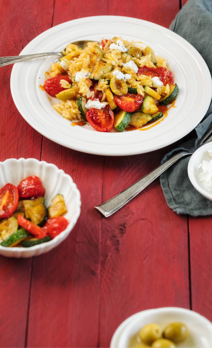 Reissalat auf einem runden Teller mit gebratenem Gemüse und Flocken von Ziegenfrischkäse