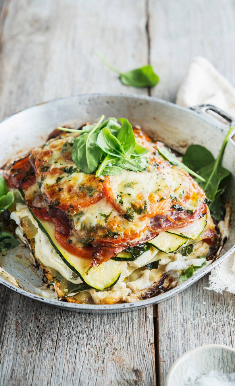Ein Stück Zucchini-Ricotta-Lasagne mit Schinken angerichtet mit frischem Basilikum auf einem Teller