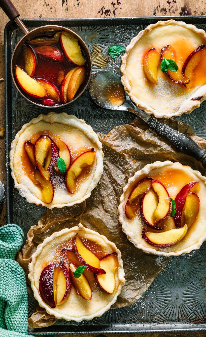 Vier Tartelettes gefüllt mit Ricottacreme und Nektarinen auf einem Backblech von oben