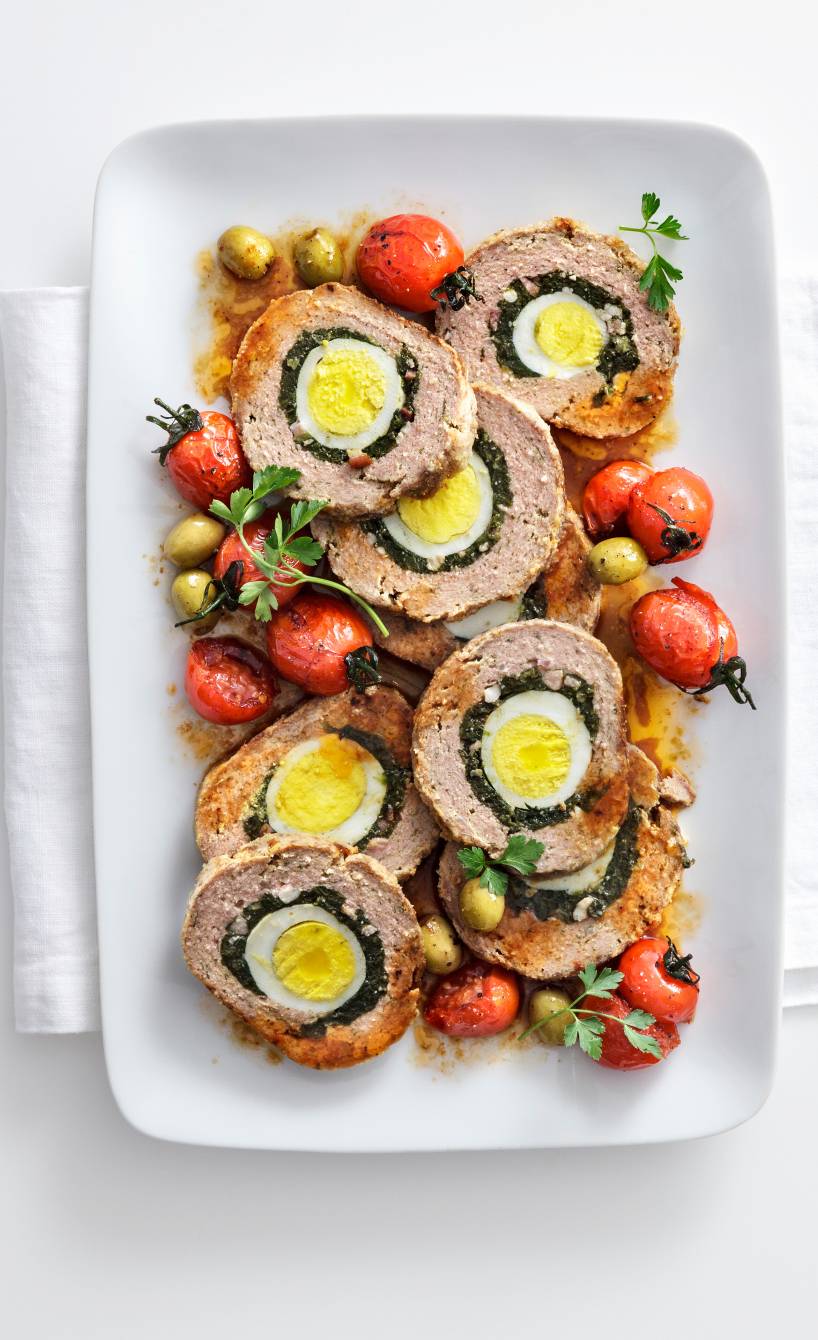 Rinderhackbraten alla pasqualina in Scheiben geschnitten angerichtet auf einer Servierplatte mit Kirschtomaten und Oliven