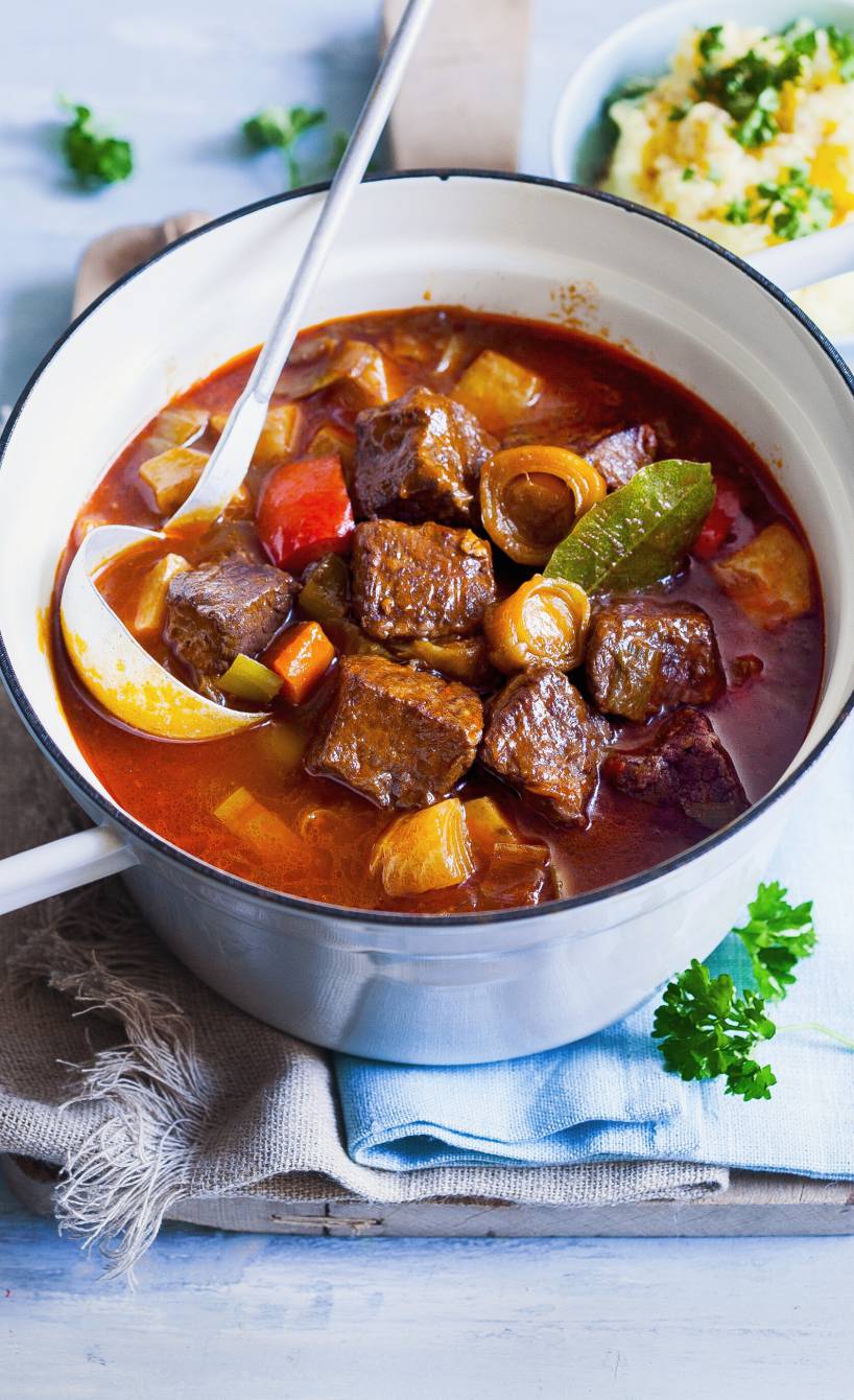 Rindfleischragout in einem Topf auf einem Tisch, daneben eine Schale mit Kartoffelstampf