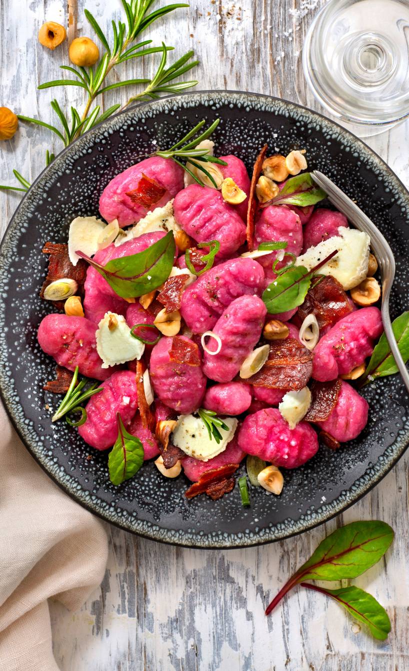 Selbstgemachte Rote Bete-Gnocchi mit Ziegenkäse, Pancetta und Haselnüssen angerichtet auf einem Teller