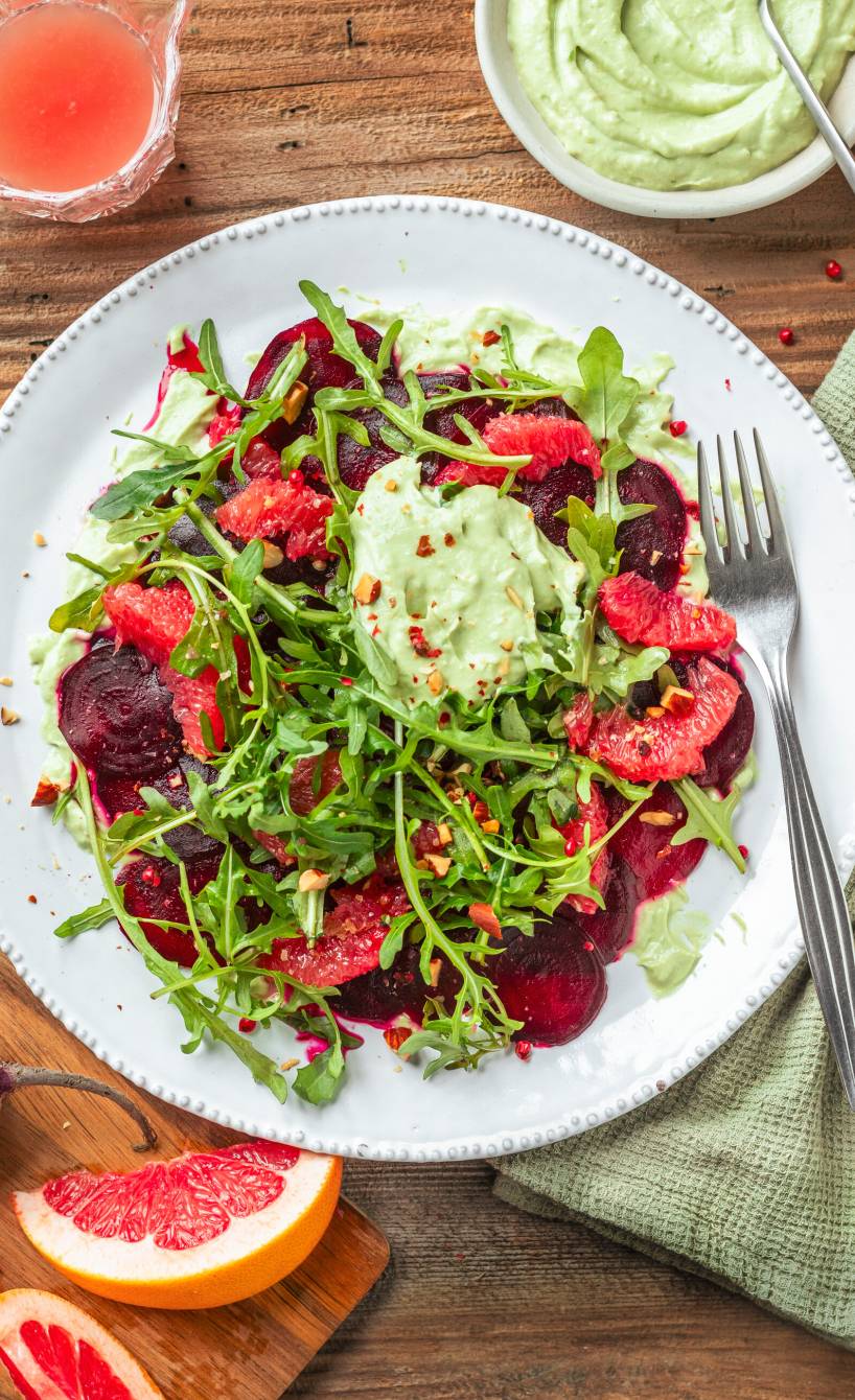 Rote-Bete-Carpaccio mit Grapefruit auf Rucola getoppt von Avocadocreme auf einem Teller