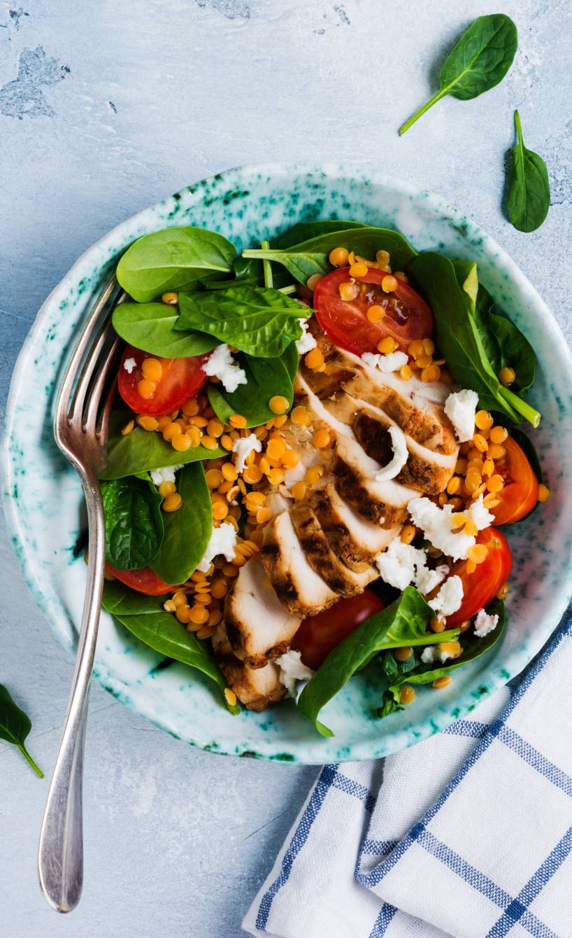 Roter Linsensalat mit Babyspinat und Tomaten getoppt von gegrillter Hähnchenbrust und Dressing in einer Salatschüssel