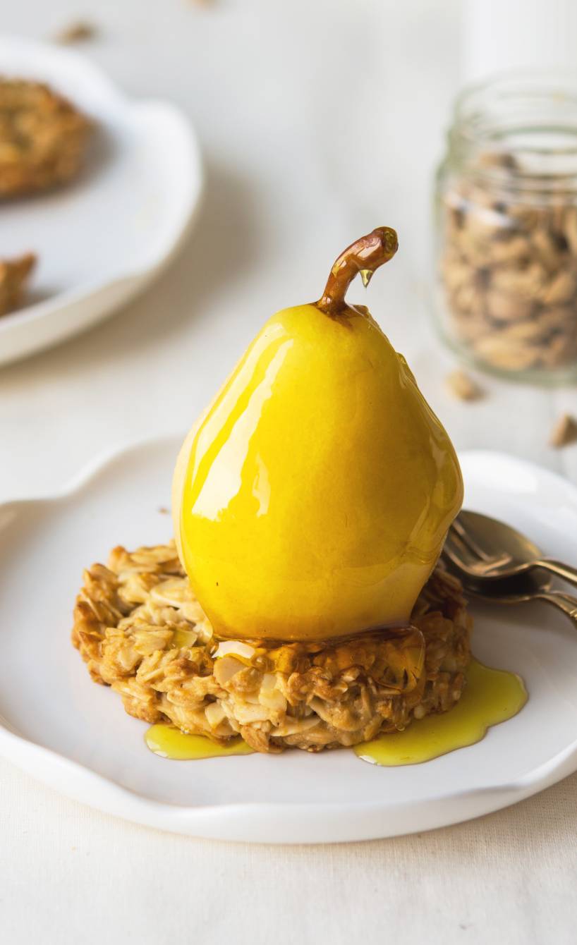 Ganze, pochierte Birne auf einem Haferkeks auf einem Dessertteller übergossen mit Safransud
