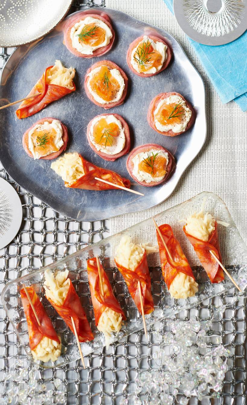 Mehrere Salami-Röllchen gefüllt mit Sellerie-Remoulade angerichtet auf einer Servierplatte auf einem Buffet