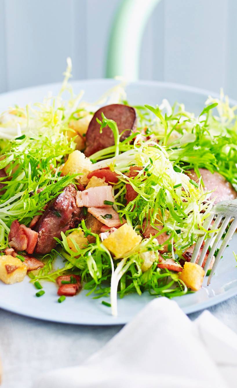 Salat mit Stücken gebratener Entenleber und Pancetta getoppt auf einem Tisch