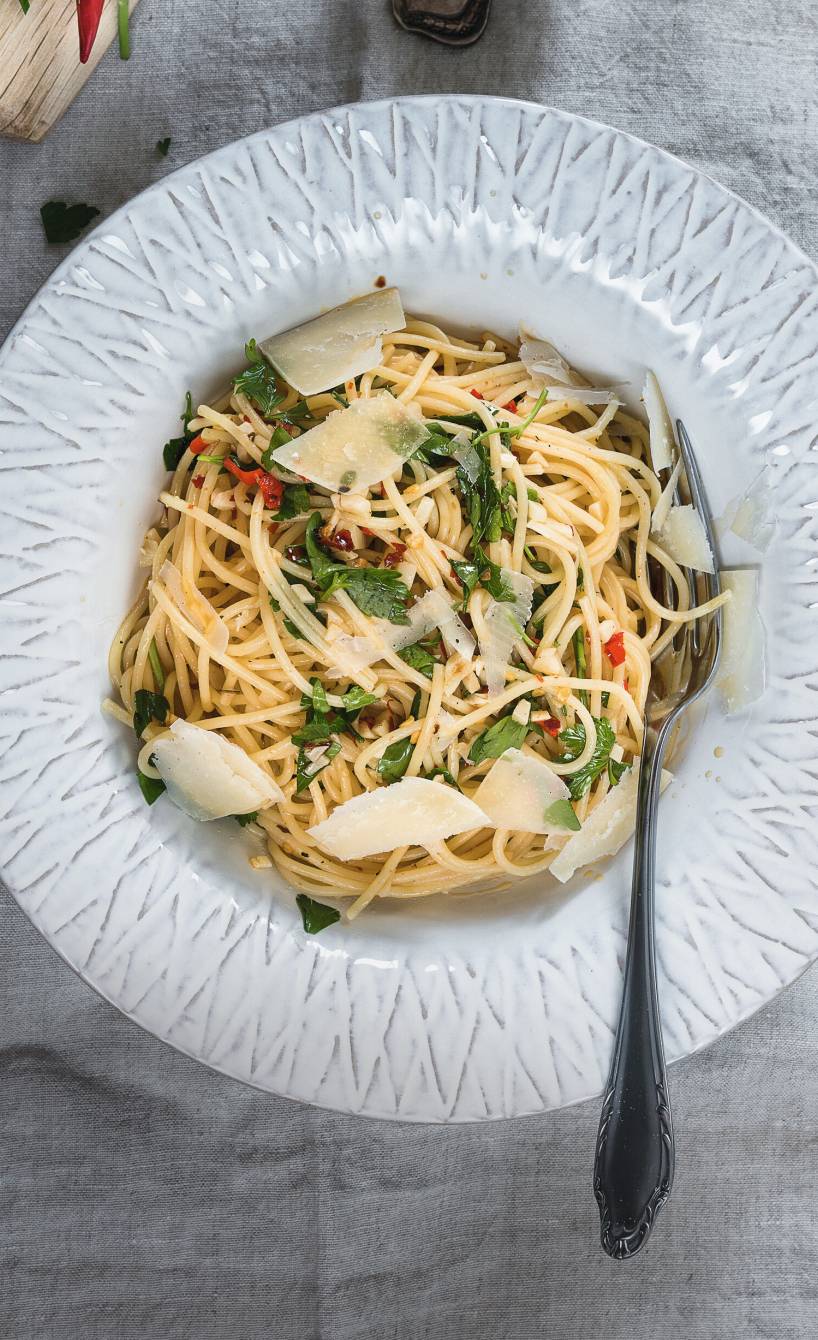 Knoblauch-Spaghetti mit Peperoncini getoppt von Parmesan und frischer Petersilie auf einem tiefen Teller