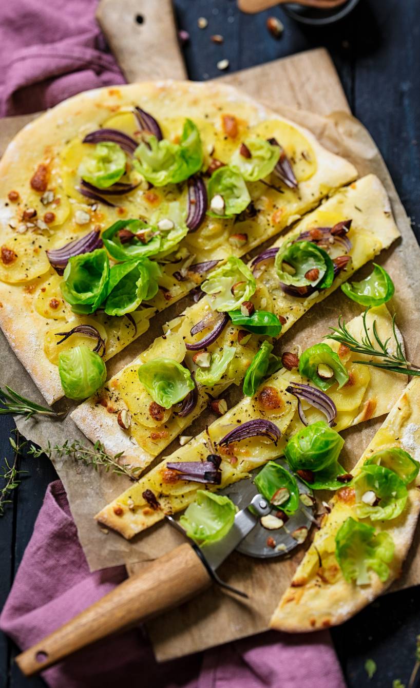 Flammkuchen mit Kartoffeln und Rosenkohl in Streifen geschnitten auf einem Holzbrett