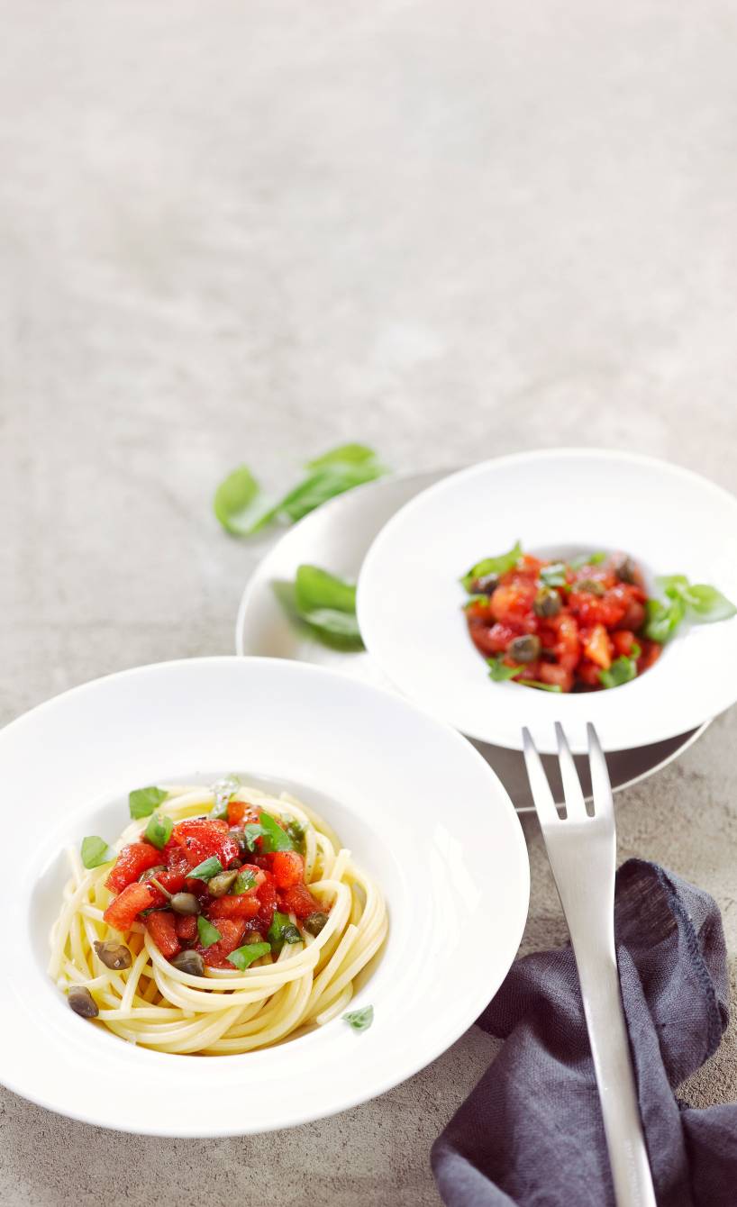Spaghetti in einem tiefen Teller getoppt mit Tomatentagout und frischen Kräutern auf einem Tisch