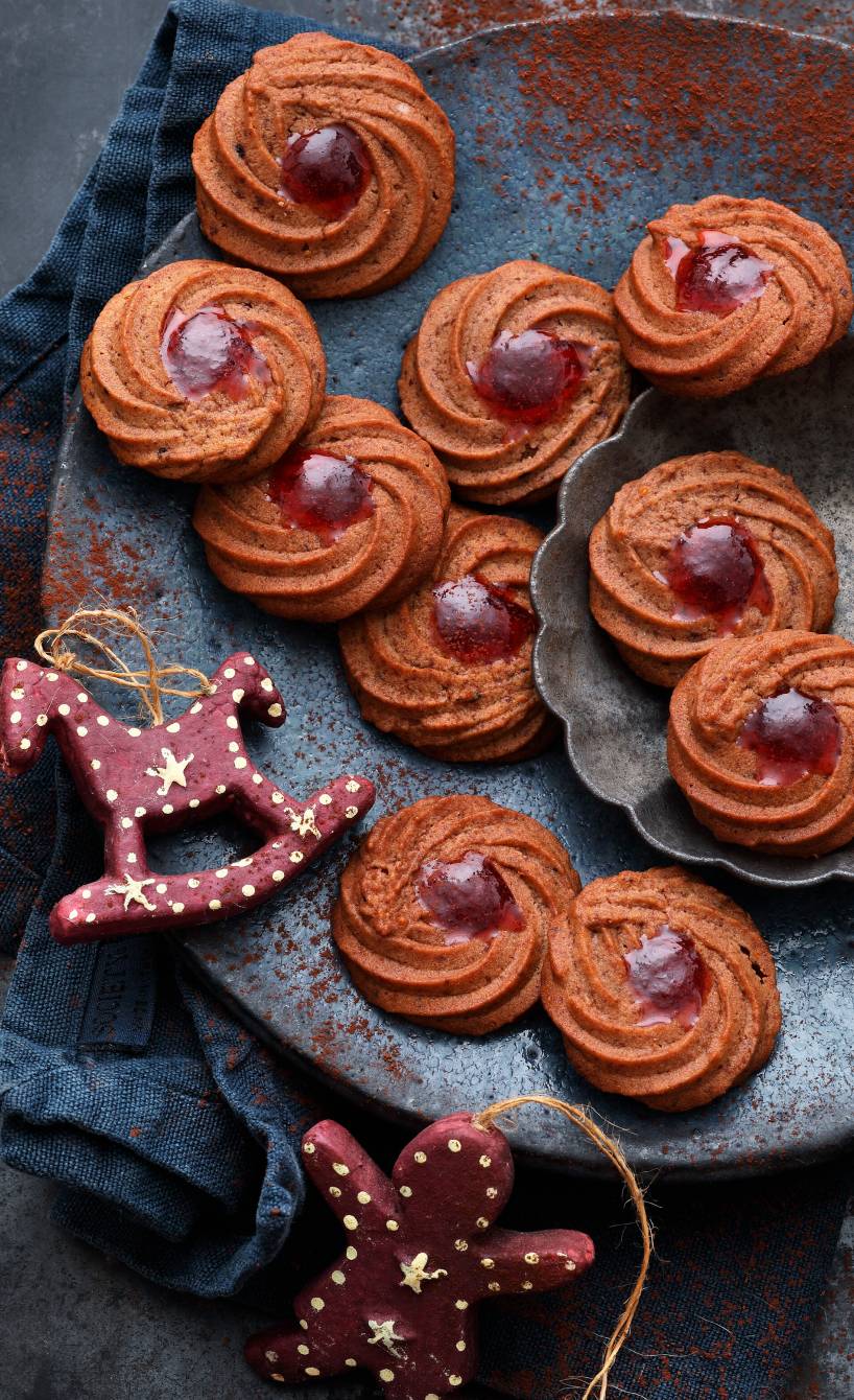 Schoko-Kirsch-Spritzgebäck in Kringeln gebacken auf einem Plätzchenteller, daneben Weihnachtsdeko