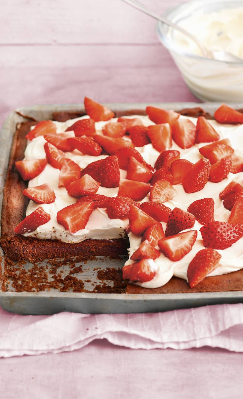 Blechkuchen aus Schokoladenboden getoppt mit mascarponecreme und frischen Erdbeeren angeschnitten auf einem Backblech